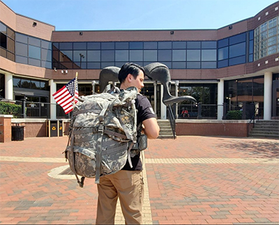 Student standing outside of commons with military style bag